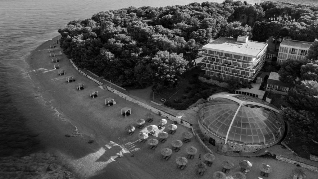 Aerial shot of Primošten beach with umbrellas and beachfront hotel in Croatia.
